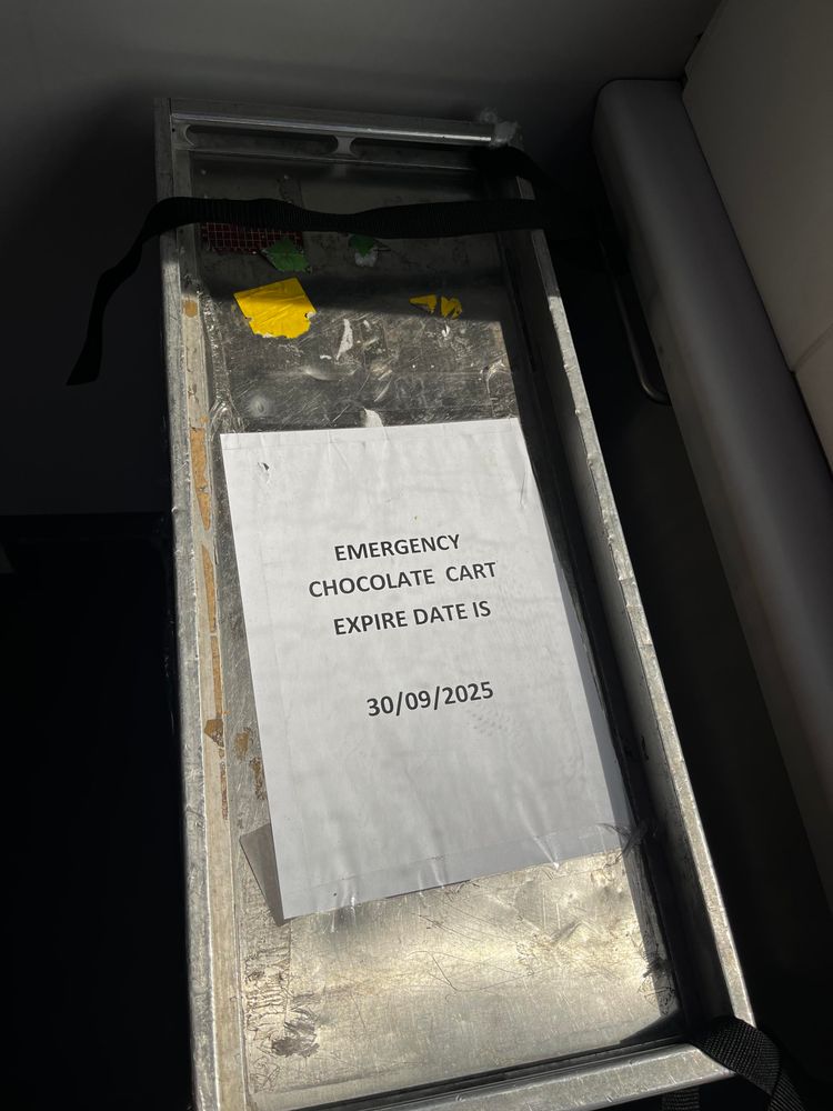 An airline-style aluminium cart. On the top is a label that says EMERGENCY
CHOCOLATE CART
EXPIRE DATE IS
30/09/2025