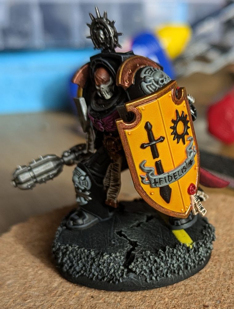 Front view of the terminator chaplain showing his shield has a star and broken sword in black and the word "fidelis" on scrollwork.