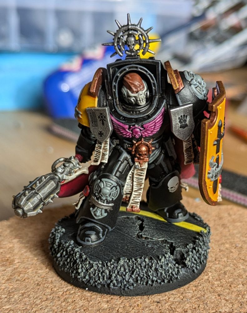An Imperial Fists terminator chaplain in yellow, black, silver and gold. He has a large shield and mace from the deathwing knight set and a partial skull mask from the reiver lieutenant.