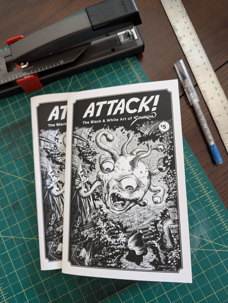 A table covered with zines, a stapler and a ruler. The makings of an Art Zine. The cover is of a beholder!! 