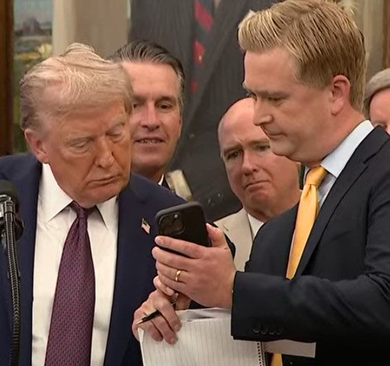 Trump being shown something on a phone.
