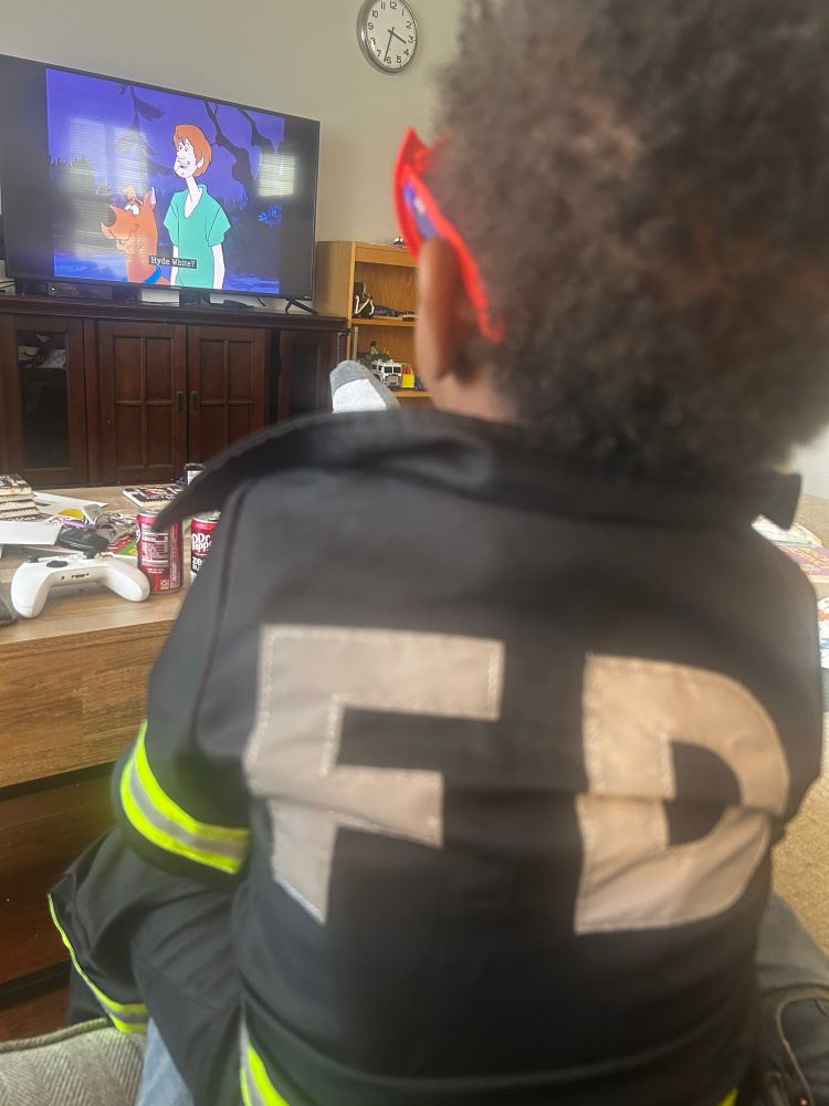 Young child watches Scooby doo cartoon while wearing fire department jacket 
