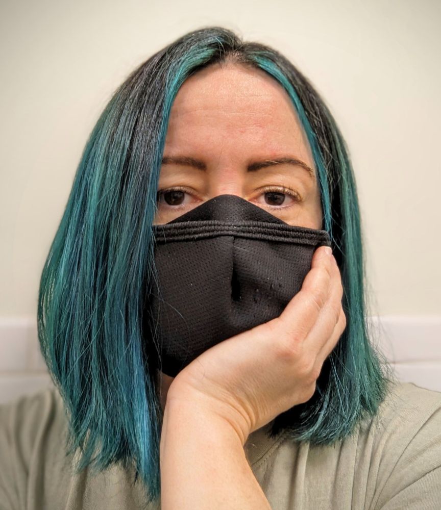 Photo of the author in a black mask. Tired eyes, but excellent teal hair cut into a fresh, shoulder-length bob.