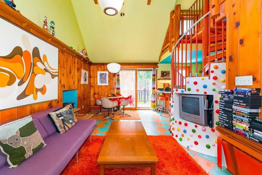 A lounge area, with a long purple sofa and a red rug over blue and peach chequered tiles