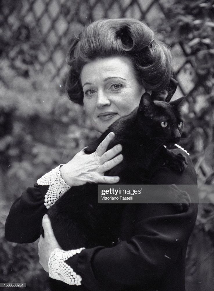 A photograph of Muriel Spark holding a black cat and smiling at the camera