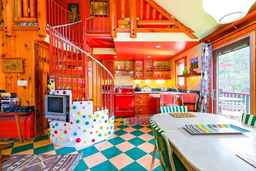Brightly-coloured interior of a motel, including: white and turquoise chequered flooring, spiral staircase, wood-panelled walls, red and yellow kitchen