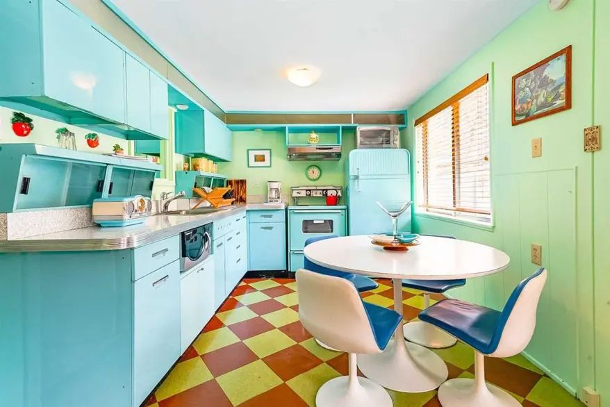 A kitchen, with matching baby blue refrigerator and cupboards. Red and yellow chequered linoleum floor. 