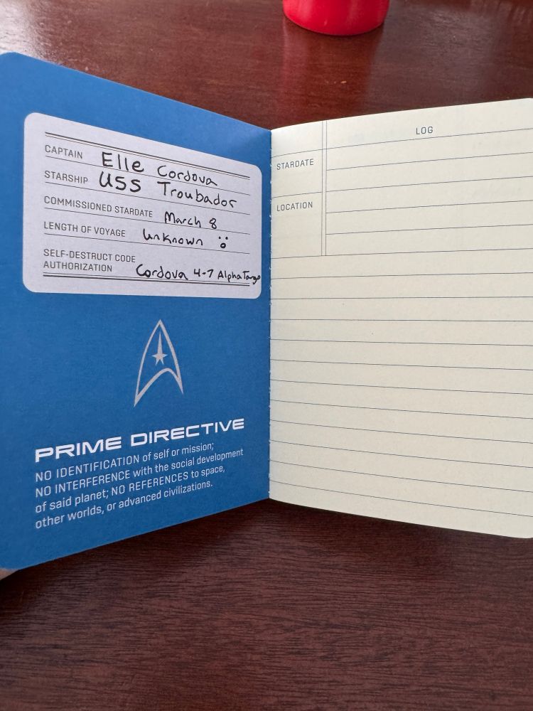 Inside the notebook the owner’s details are displayed. Captain: Elle Cordova. Starship: USS Troubadour. Commissioned Date: March 8. Length of Voyage: unknown. Self Destruct Code Authorization: Cordova 4-7 Alpha Tango.
