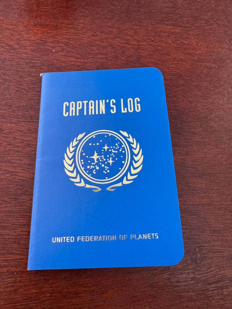 A blue notebook titled “Captain’s Log” that displays the United Federation of Planets logo from Star Trek on the front cover.