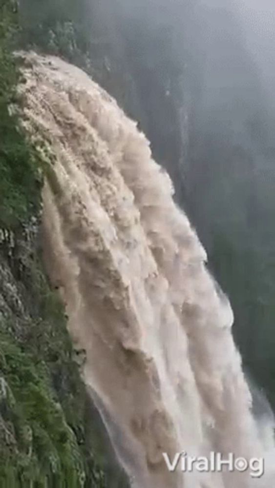 a large waterfall is coming down a cliff in the mountains .