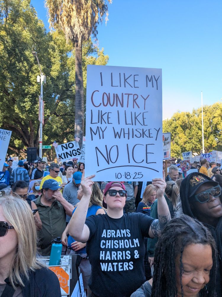 SacramentoNoKings protest. Protestor hiding a sign that reads 'I like my country like I like my whiskey, NO ICE!'