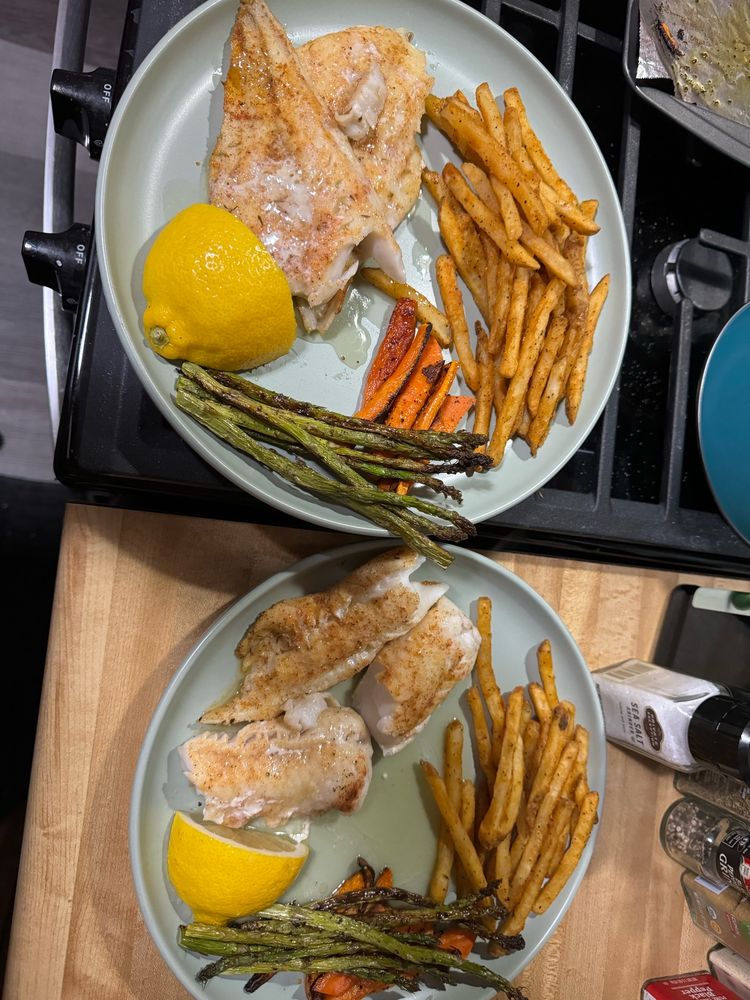 A picture of baked cod with fries, baked asparagus and carrots as a side, and a lemon on the plate. 