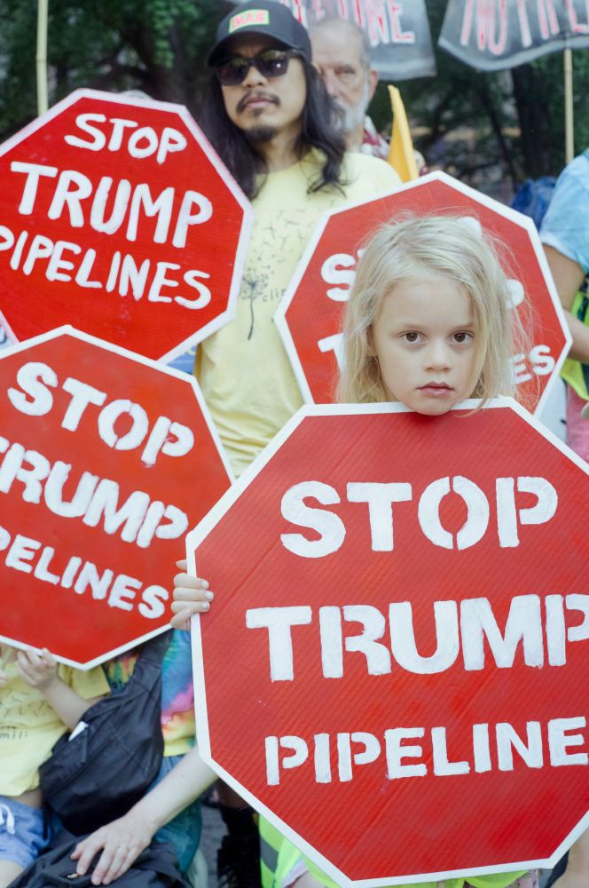 A child holds a red stop sign that reads STOP TRUMP PIPELINES in a crowd