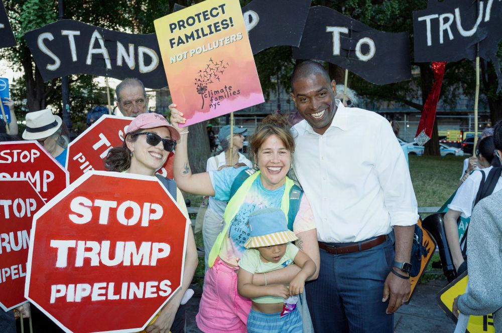 Antonio Delgado stands with two moms and a toddler, a sign that says Protect Families, not polluters, and a red stop sign that says Stop Trump Pipelines in white
