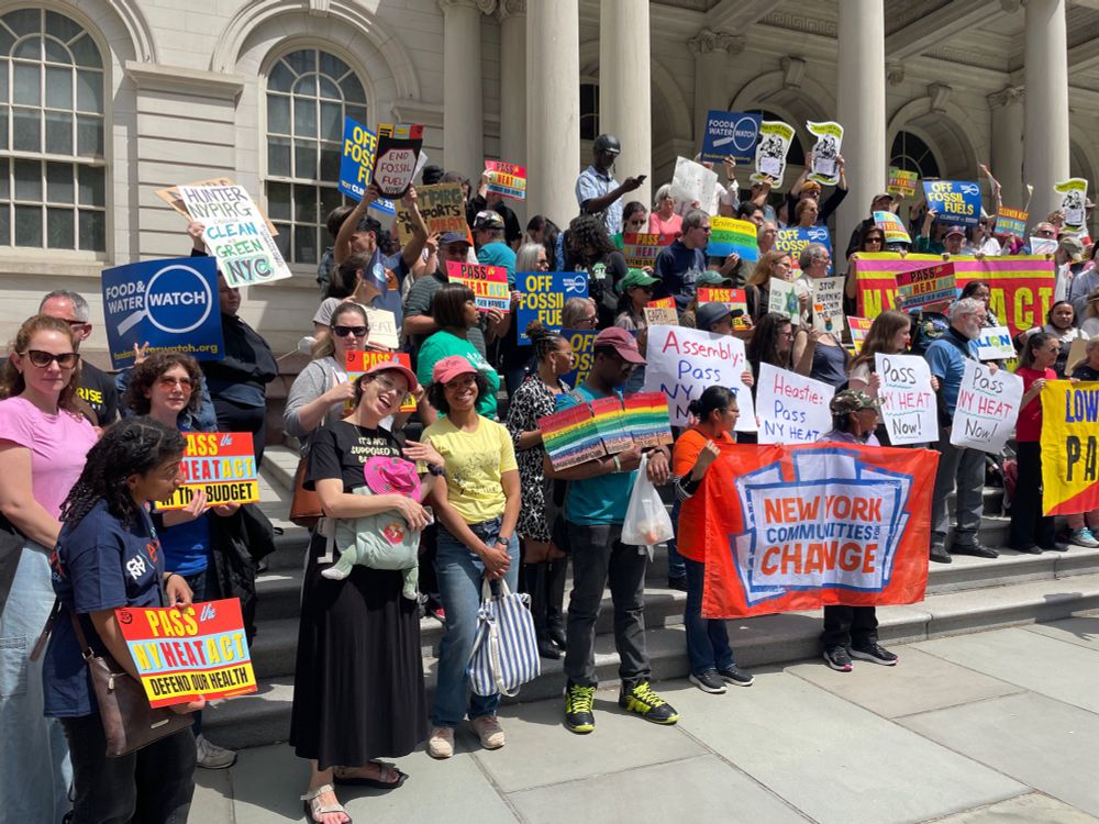 Crowd of people holding signs on the steps of NYC City Hall for the NY Heat Act. 