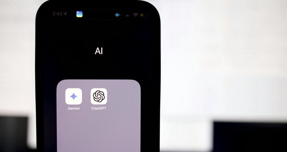 The image is of an Apple iPhone with the screen unlocked showing a folder called ‘AI’, in which is Google’s Gemini and OpenAI’s ChatGPT.