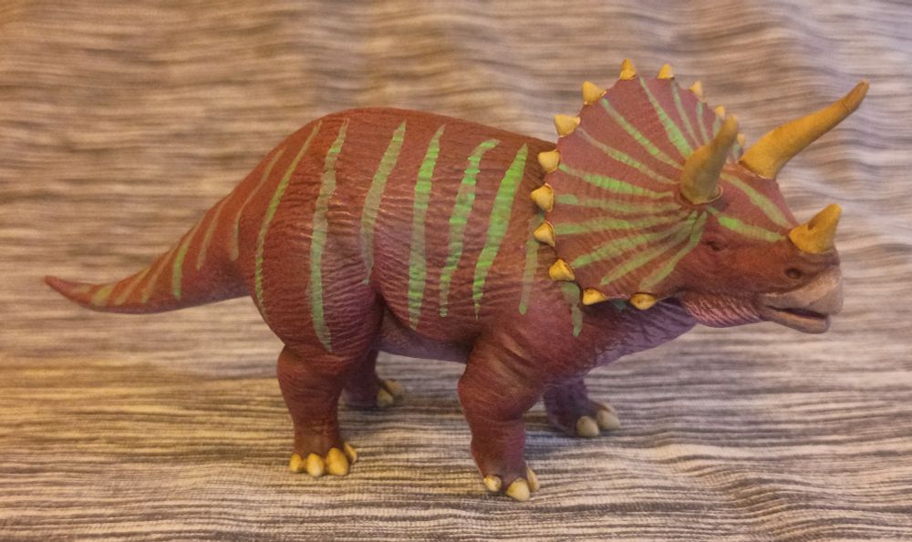 A purple triceratops with pink underbelly and pale green tiger stripes. She has a powerful tail, 3 significant horns, and 4 strong legs. Say she ISN'T a femme fatale at your own risk...