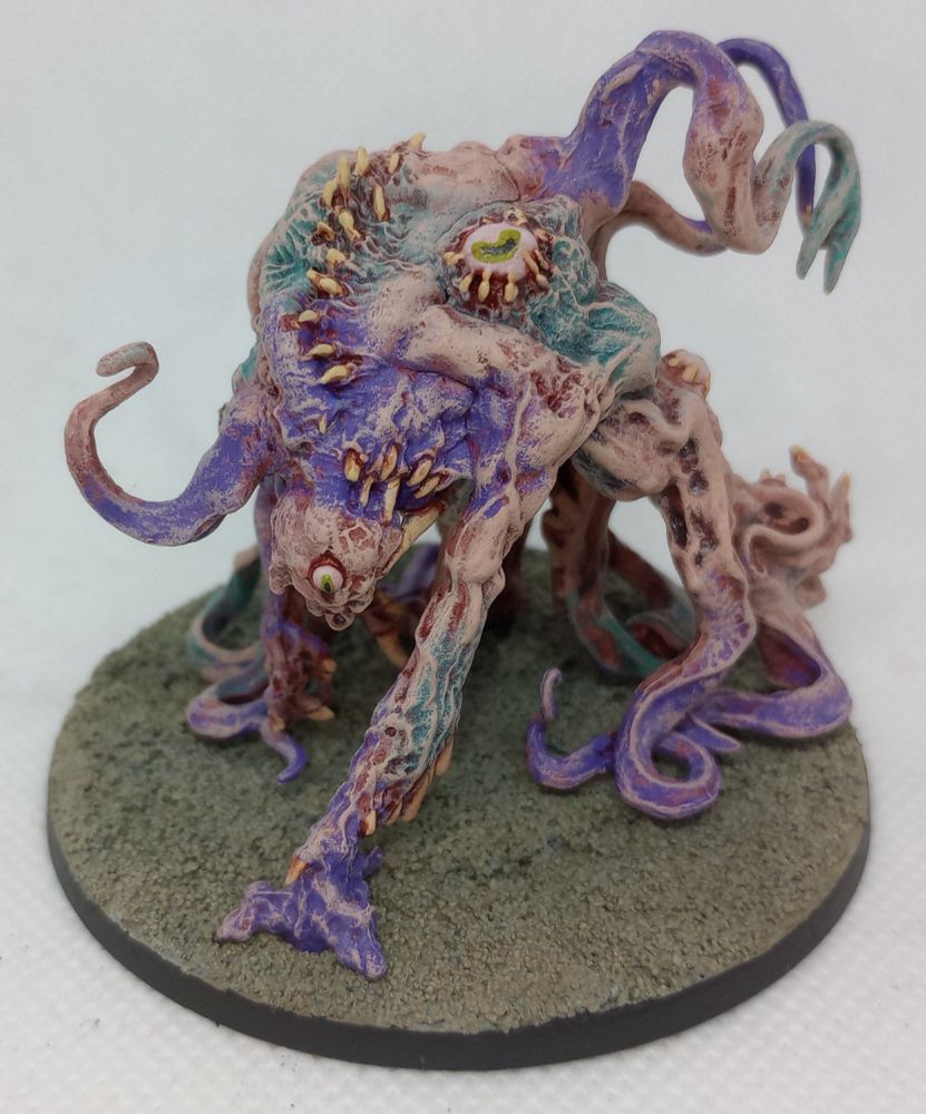 A writhing fleshy mass of pinkish flesh with purple and teal accents with bloodshot eyes and claws puncturing out of the flesh in areas.