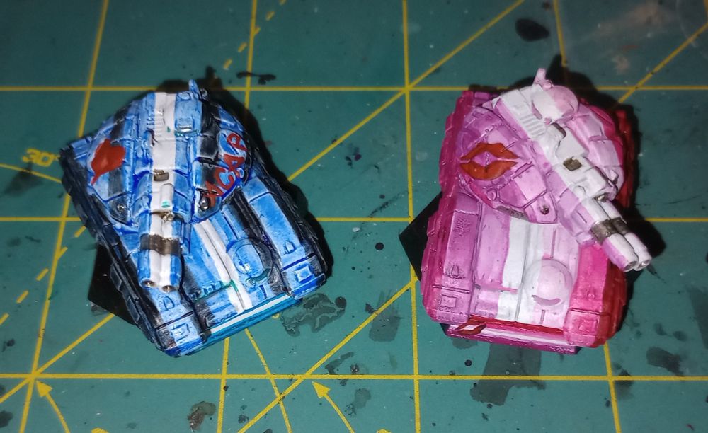 2 Battletech tanks painted in the classic leather/bdsm pride flag and lipstick lesbian pride flag. The leather tank has A C A B emblazoned on the turret.