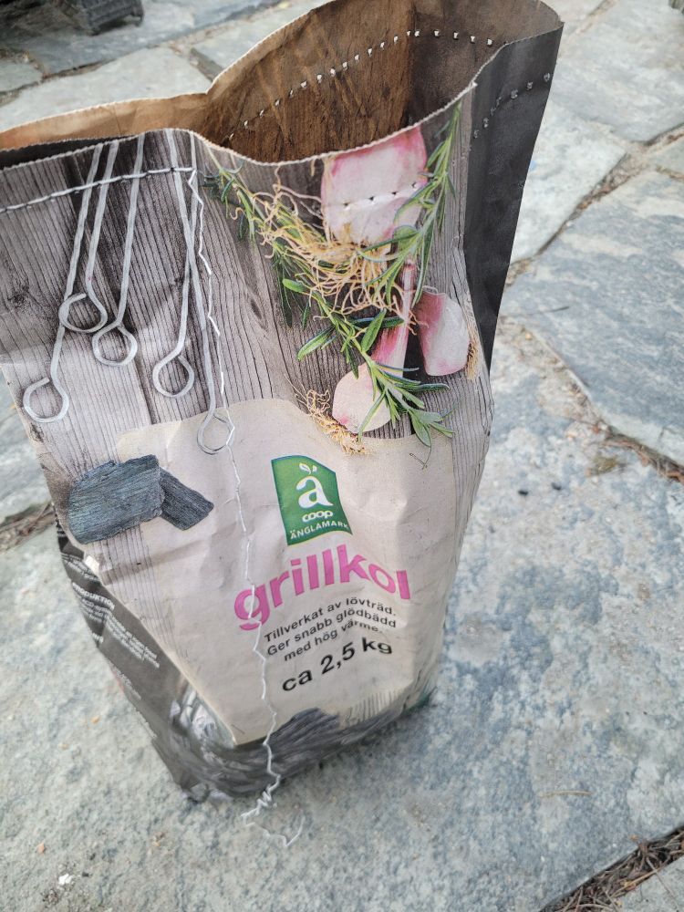 Påse med grillkol, där sömmen som försluter den elegant repats upp genom att dra i tåtarna. 