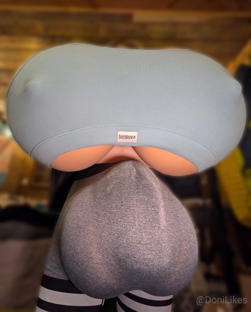 Waist high picture looking up at a person with large breasts and bulge in their pants.  They are fully clothed with a teal bra and grey yoga pants.  The top of their head is barely visible.