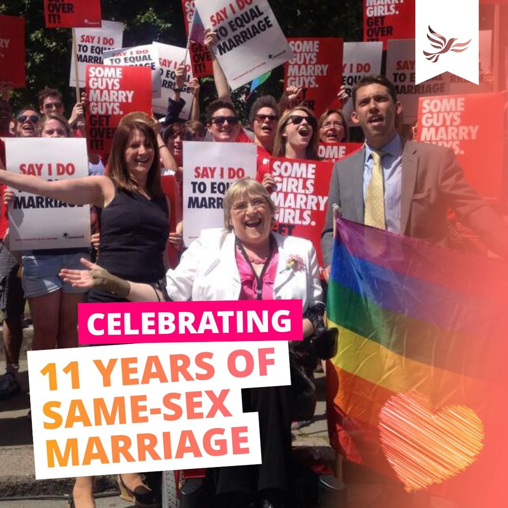 The text Celebrating 11 Years of Same-Sex Marriage, in pink, white and orange, on the background of a sunny picture of cheering people, with, in the foreground, Lynne Featherstone (Former Equalities Minister), Sal Brinton (Former President of the Liberal Democrats) and Adrian Hyryylainen-Trett (Former Chair of LGBT+ Liberal Democrats) cheering.  Adrian is waving a rainbow flag.  In the background, a large cheering crowd in white, black and red Stonewall colours wave placards saying 'SAY I DO TO EQUAL MARRIAGE', 'Some guys marry guys. Get over it!' and 'Some girls marry girls. Get over it!'