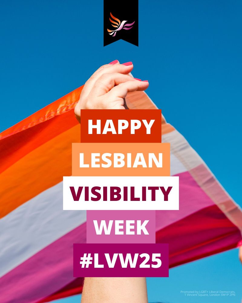 The words 'Happy Lesbian Visibility Week #LVW25' in white and dark purple on the colours of the Lesbian flag, with a pink nail-varnished white hand holding a Lesbian flag against a bright blue sky in the background.  On the top is a black banner with the Lib Dem bird-of-liberty in Lesbian colours.