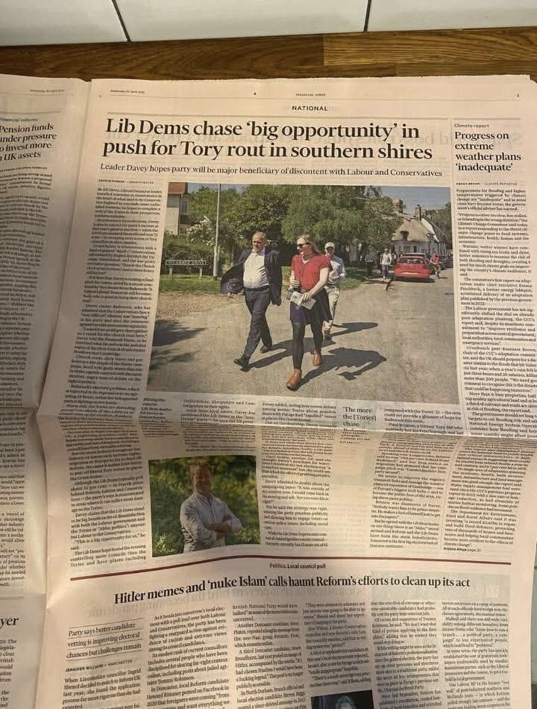 A low-resolution picture of page 3 of today's Financial Times, a paper famously printed on slightly pink paper. The main headline is 'Lib Dems chase 'big opportunity' in push for Tory rout in southern shires', with the subtitle 'Leader Davey hopes party will be major beneficiary of discontent with Labour and Conservatives' just visible.  A very large picture is in the centre, of a besuited Sir Ed Davey MP walking down a village lane in bright sunshine, alongside a woman wearing sunglasses, a red short-sleeved top, a black skirt and leggings, and brown boots.