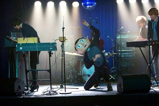 A person with a large fake head fronts a rock band