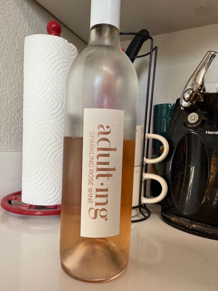 An opened bottle of sparkling rose wine. The label reads “Adulting”
