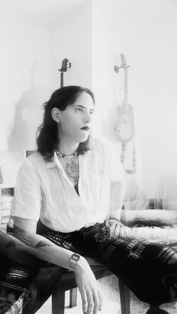 Selfie blanco y negro, sentada en una silla. Ambas manos están apoyadas en mis piernas, miro hacia el infinito.