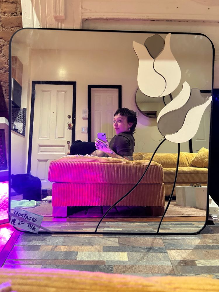 Alyssa smirking in the reflection of a square, post modern mirror featuring two large tulips 