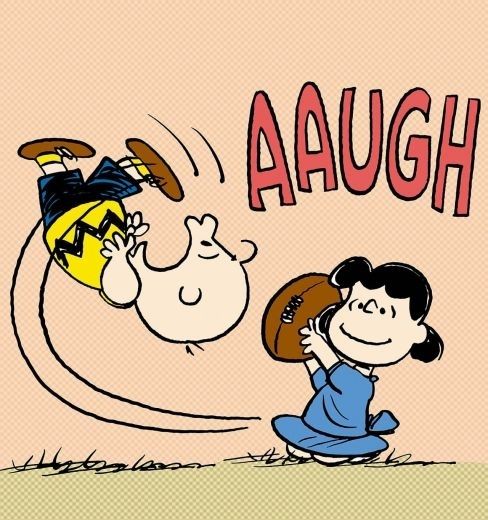 A panel of a Peanuts comic showing Lucy smiling as she snatches the football from its place on the ground, causing Charlie Brown to miss his kick and cry "AAUGH" as he falls backward.