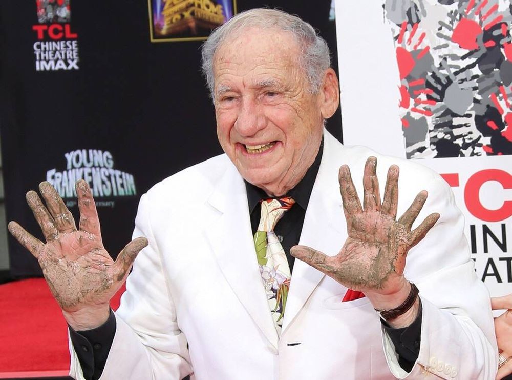 Mel Brooks in a white suit with wet cement on his hands, and a prosthetic 6th finger on his left hand