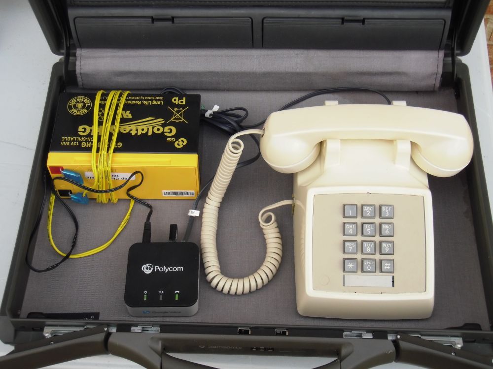 Photograph of a portable VoIP telephone system inside a briefcase. A lead-acid 12 volt battery powers an OBi200 analog telephone adapter. It is fitted with an OBiWiFi attachment to allow placing calls over Wi-Fi networks. The telephone adapter is connected to an ivory colored Western Electric 2500 series telephone, circa 1980 vintage.