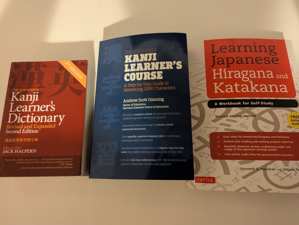 Three books: The Kanji Learner's Dictionary, the Kanji Learner's Course, and Learning Japanese Hiragana and Katakana arranged on a white table