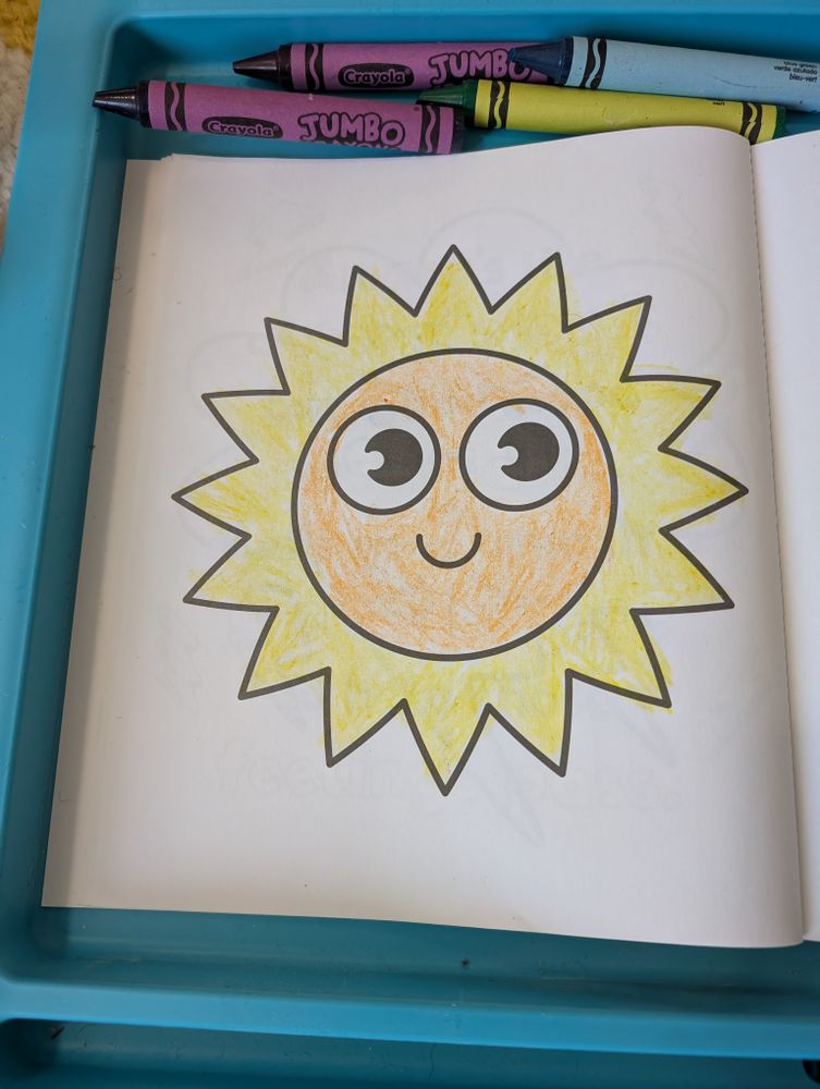 A photo of a page from a colouring book. It's a big, simple drawing of the sun with a happy smiling face. I coloured the middle orange and the outside yellow!