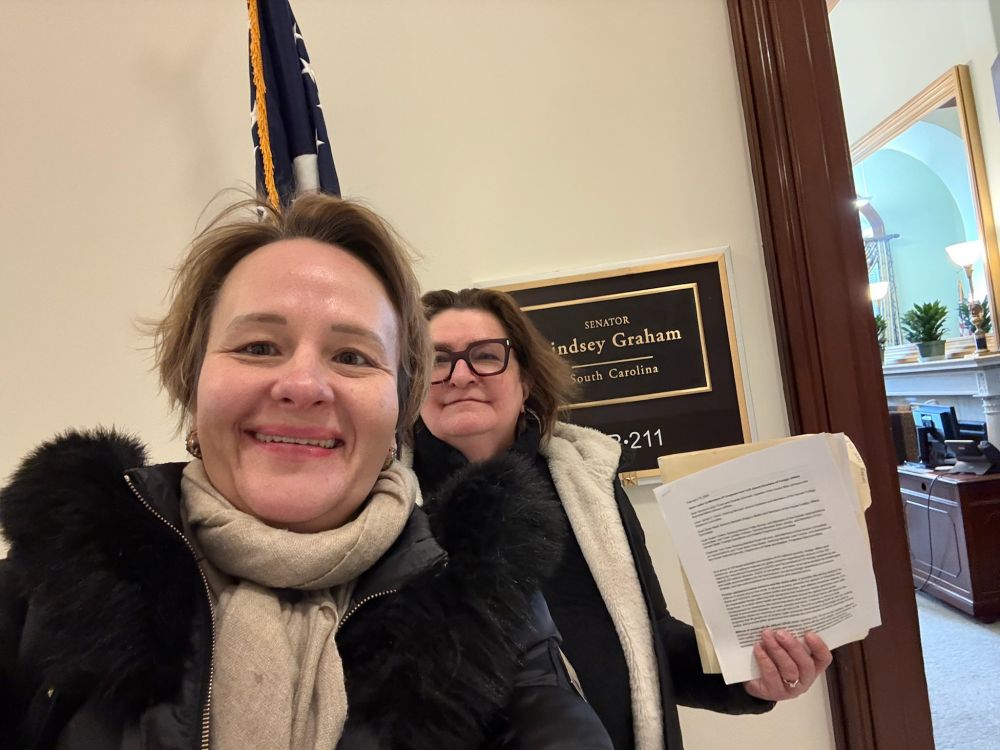 Two scholars standing outside Senator Lindsey Graham's office delivering a letter. Interior of office visible in background.