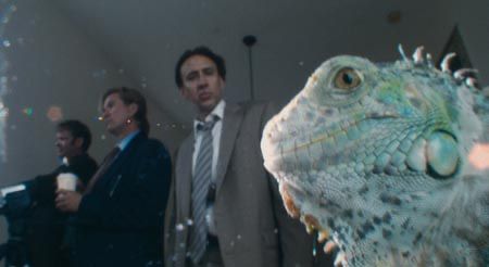 Screenshot from Bad Lieutenant: Port of Call New Orleans. It’s a close up of an iguana. Nicholas Cage and Val Kilmer are in the background, out of focus.