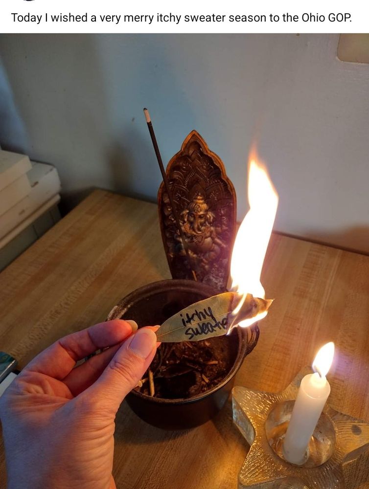 In image:  a bay leaf with the words "itchy sweater" burning over a cauldron. An incense stick is burning in a Ganesha holder, while a white candle burns in a glass star shaped holder. 