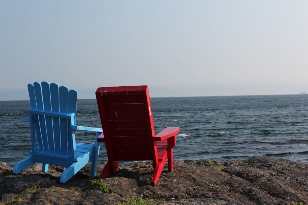 Chairs on beach, next to Dallas Road in Victoria, BC. They look south across the Salish Sea towards Washington State, obscured by the distant haze.