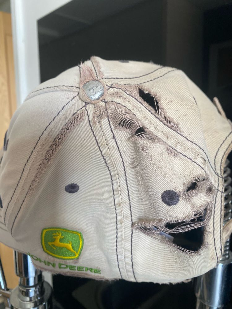 Threadbare holes worn through in a John Deere hat.