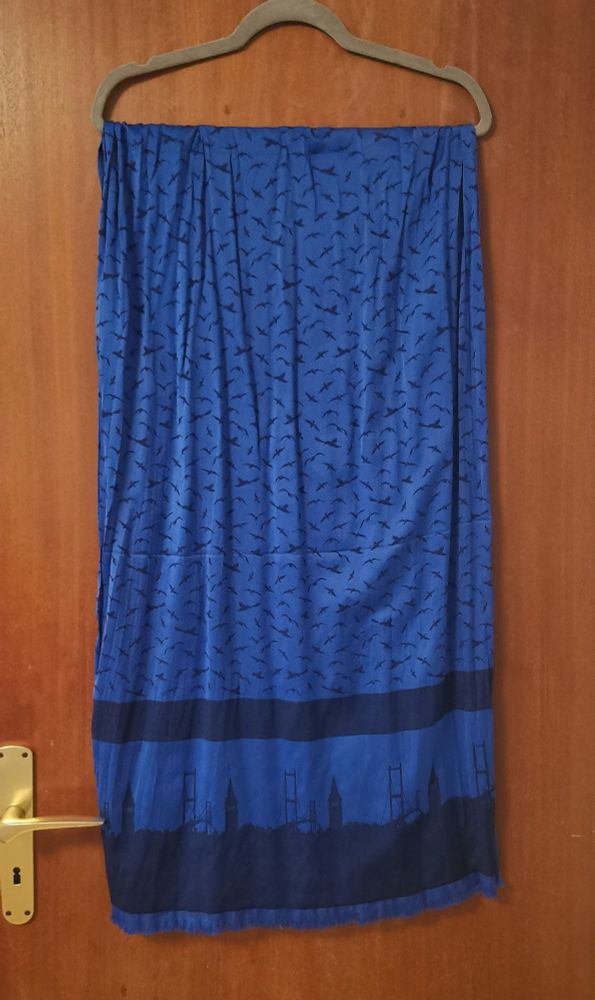 Leuchtend blaues Tuch mit dunkelblauen kleinen Vögeln. An den Enden des Tuchs ist in dunkelblau eine Skyline und darüber ein dunkelblaue Streifen.