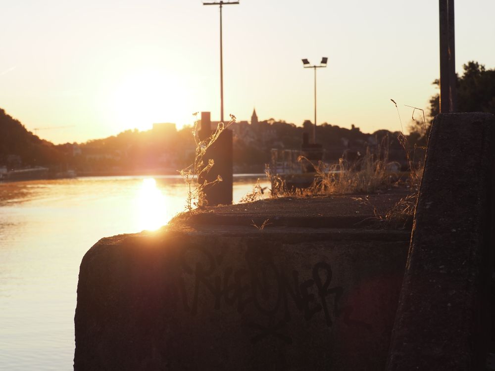 Lever de soleil sur Conflans St Honorine (78) vue depuis la rive faisant face à la ville
Au premier plan le quai avec derrière la Seine et le reflet du soleil ; au fond la vile de Conflans  (photo prise le 4 07 2025)
