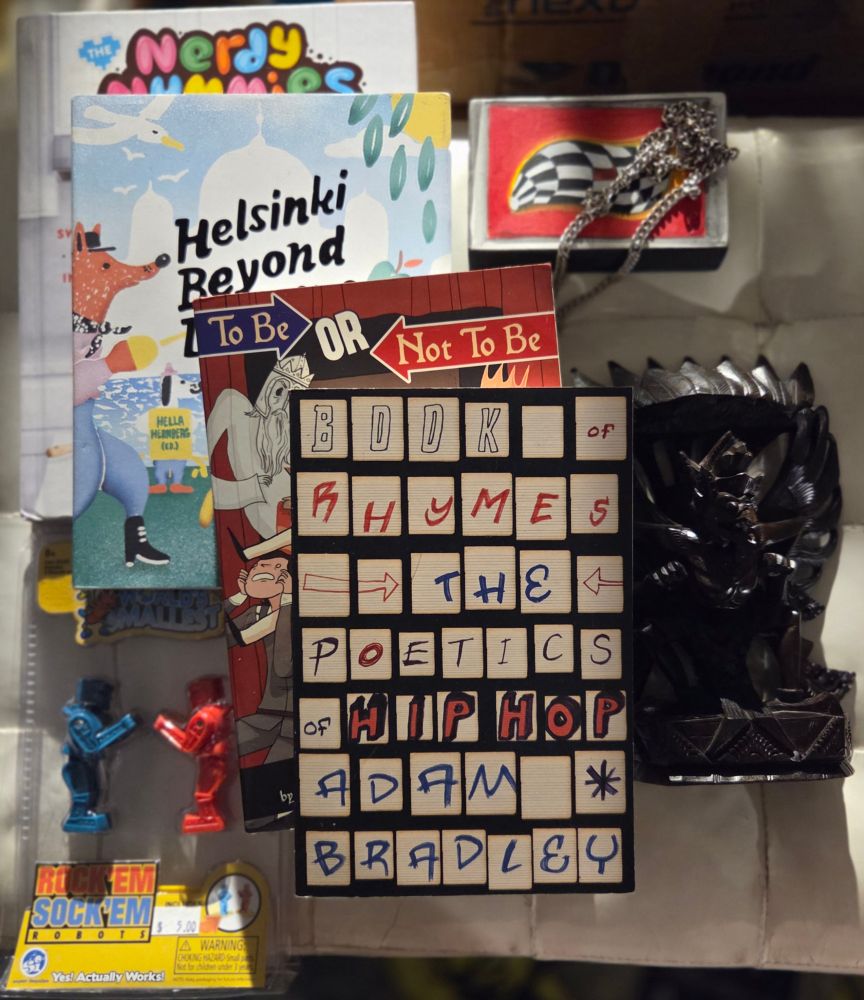 Thrift haul for 8/5/25: 4 books (NERDY NUMMIES by Rosanna Pansino, HELSINKI BEYOND DREAMS by Hella Hernberg, TO BE OR NOT TO BE by Ryan North, BOOK OF RHYMES: THE POETICS OF HIP-HOP by Adam Bradley), a World's Smallest Rock 'Em Sock 'Em Robots set, a canvas print of a black & white checkered blob against a red background, a short chain necklace & a ~8" tall wooden carving of the Hindu deity Garuda.