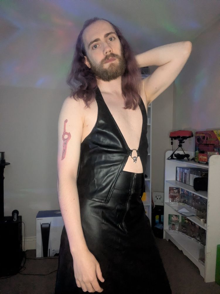 Blank Master wearing a faux leather halter top and faux leather skirt. Multi-coloured caustics are being projected onto the scene.