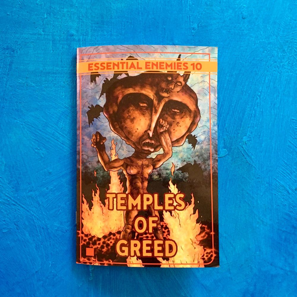 A half-letter digest-sized staplebound zine entitled Essential Enemies 10: Temples of Greed liesup on a bright blue surface. The cover illustration depicts an animated bronze statue in a cave surrounded by fire, lava, and flying bats.