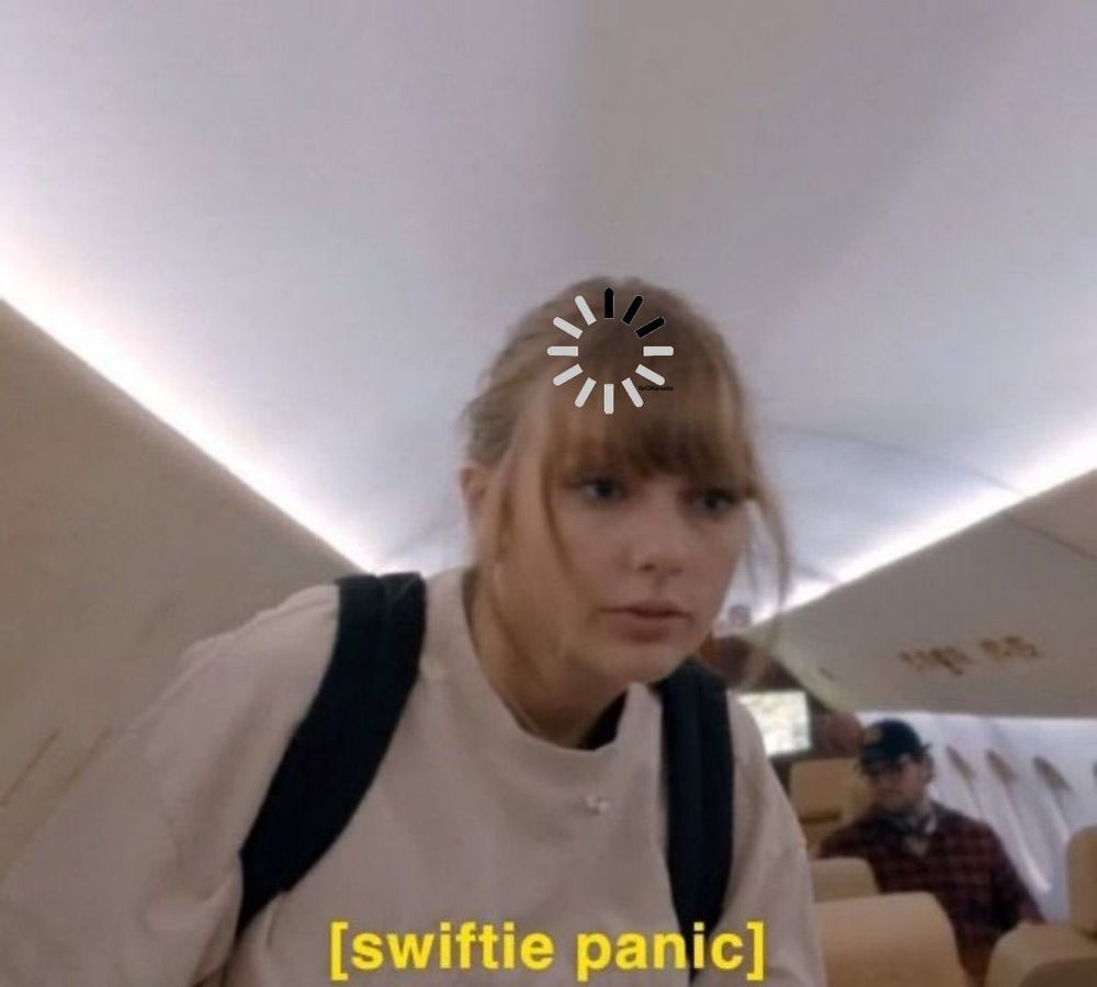 an image of taylor swift looking stressed on a plane . a buffering symbol is edited onto her head and there is a caption in yellow font that reads “ [ swiftie panic ] “