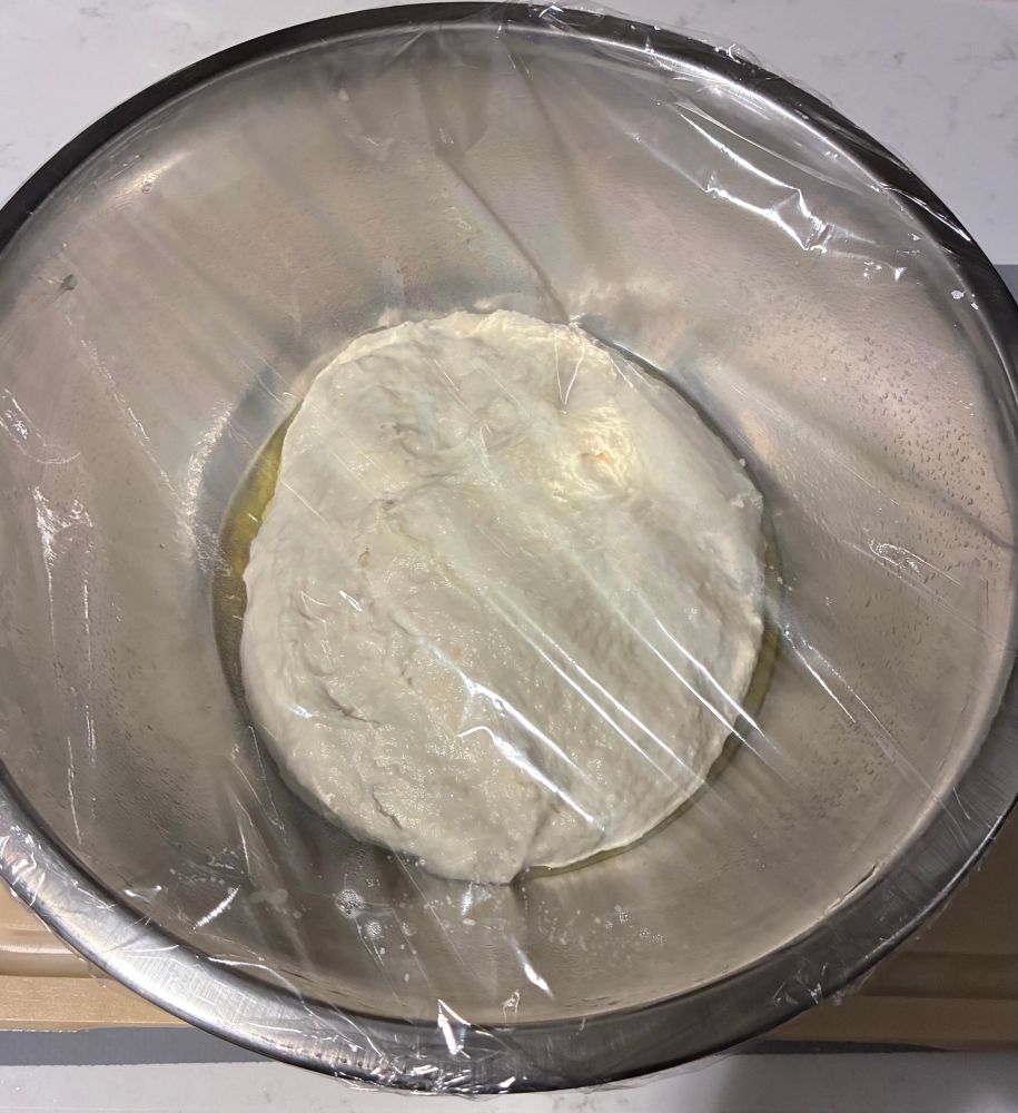 a ball of bread dough in a metal bowl covered in plastic wrap 