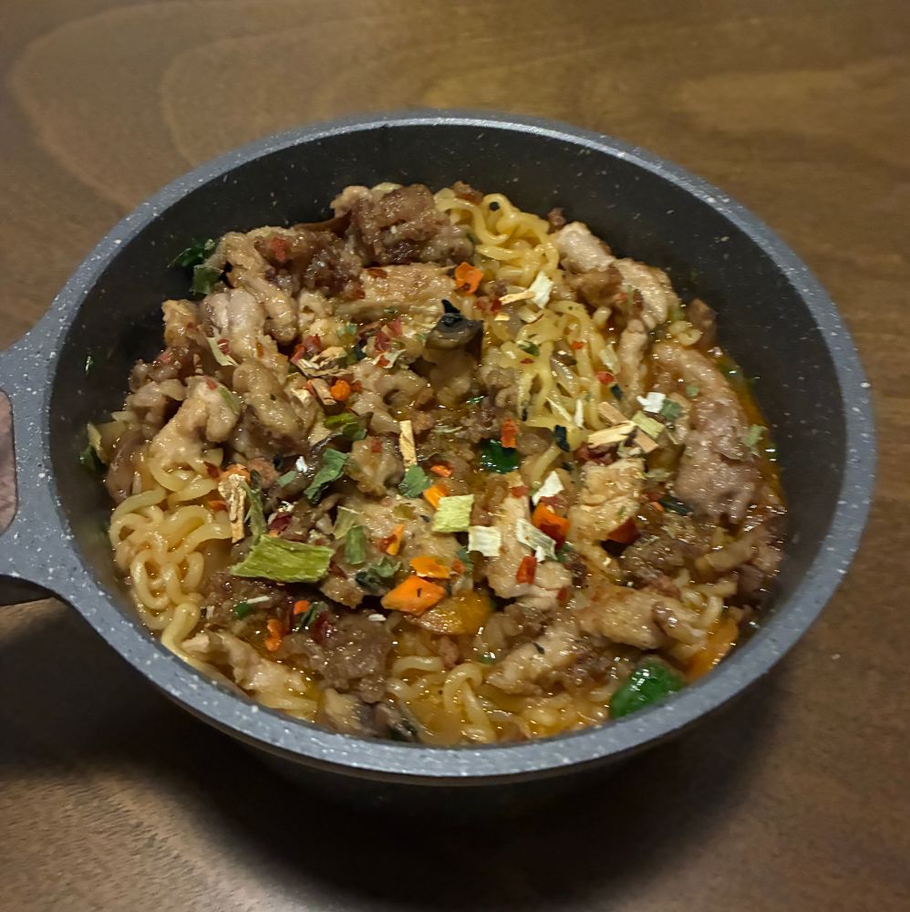 a pot of shin ramyun noodles topped with some thinly shaved fried pork